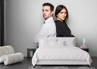 Concept of partnership in business. Young man and woman standing back-to-back with crossed hands against gray background Wall mural